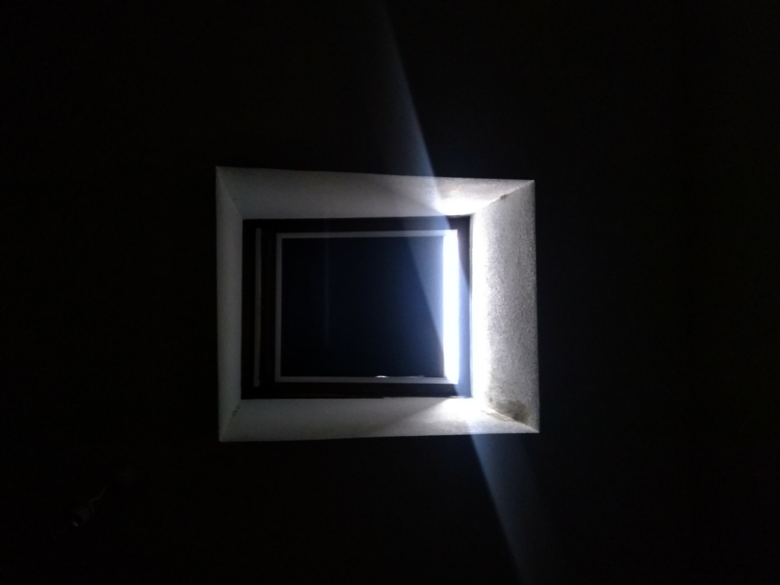 Photo d'un Velux®, fermé, vu d'en-dessous. Seul un rayon de lumière réussit à passer à travers.