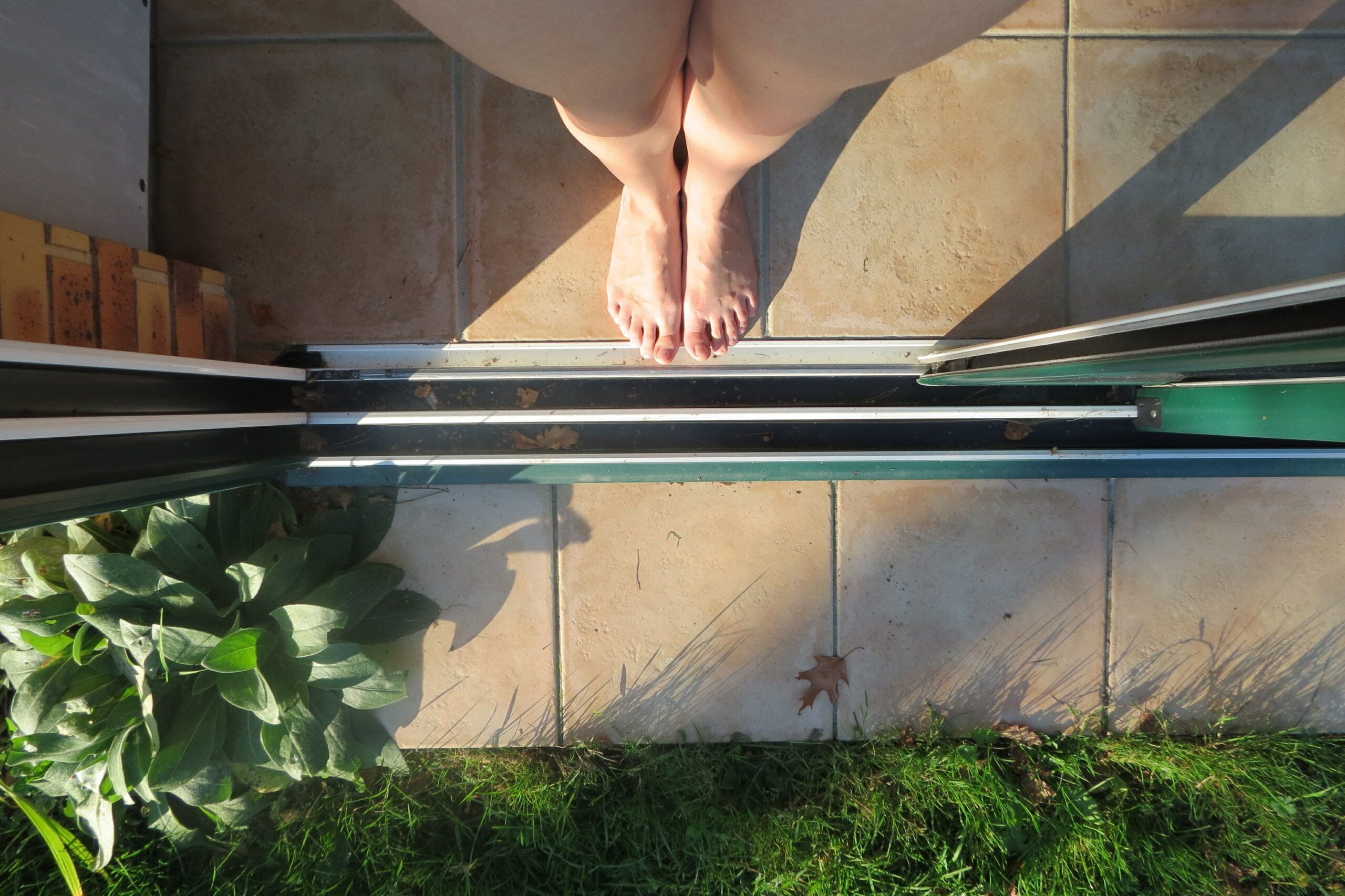 Vue du dessus. Mes pieds au bord de la porte fenêtre, à l'intérieur, prêts à sortir, immobiles.