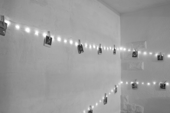 Une guirlande lumineuse accrochée au mur avec des photos épinglée avec des pinces à linge dessus. L'image est en noir et blanc.