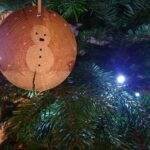 Entre les branches du sapin, une décoration faite main. Un bonhomme de neige peint sur une rondelle de bois.