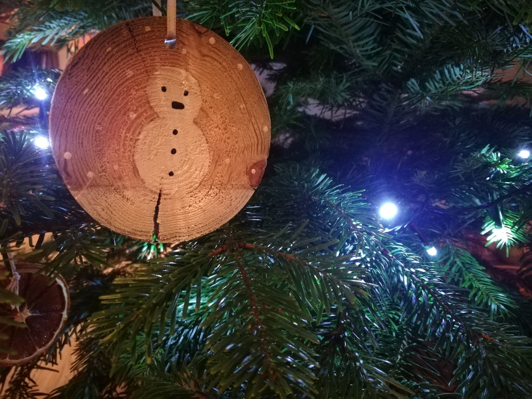 Entre les branches du sapin, une décoration faite main. Un bonhomme de neige peint sur une rondelle de bois.