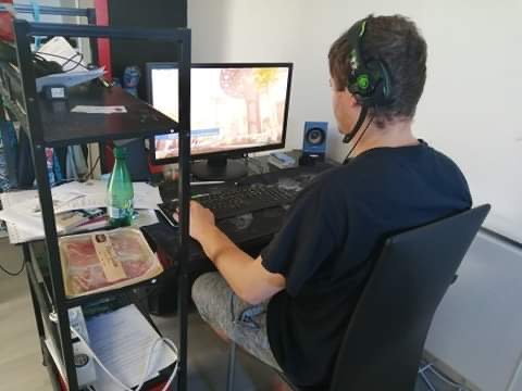 Photo d'un homme d'une trentaine d'années en train de jouer à des jeux vidéo en réseau sur son ordinateur de bureau. Il tourne le dos à la caméra, a les yeux rivés sur son écran et porte un casque audio. À sa gauche on peut voir un paquet de charcuteries qui montre qu'il ne prend pas le temps de se nourrir correctement parce qu'il souhaite jouer autant que possible.