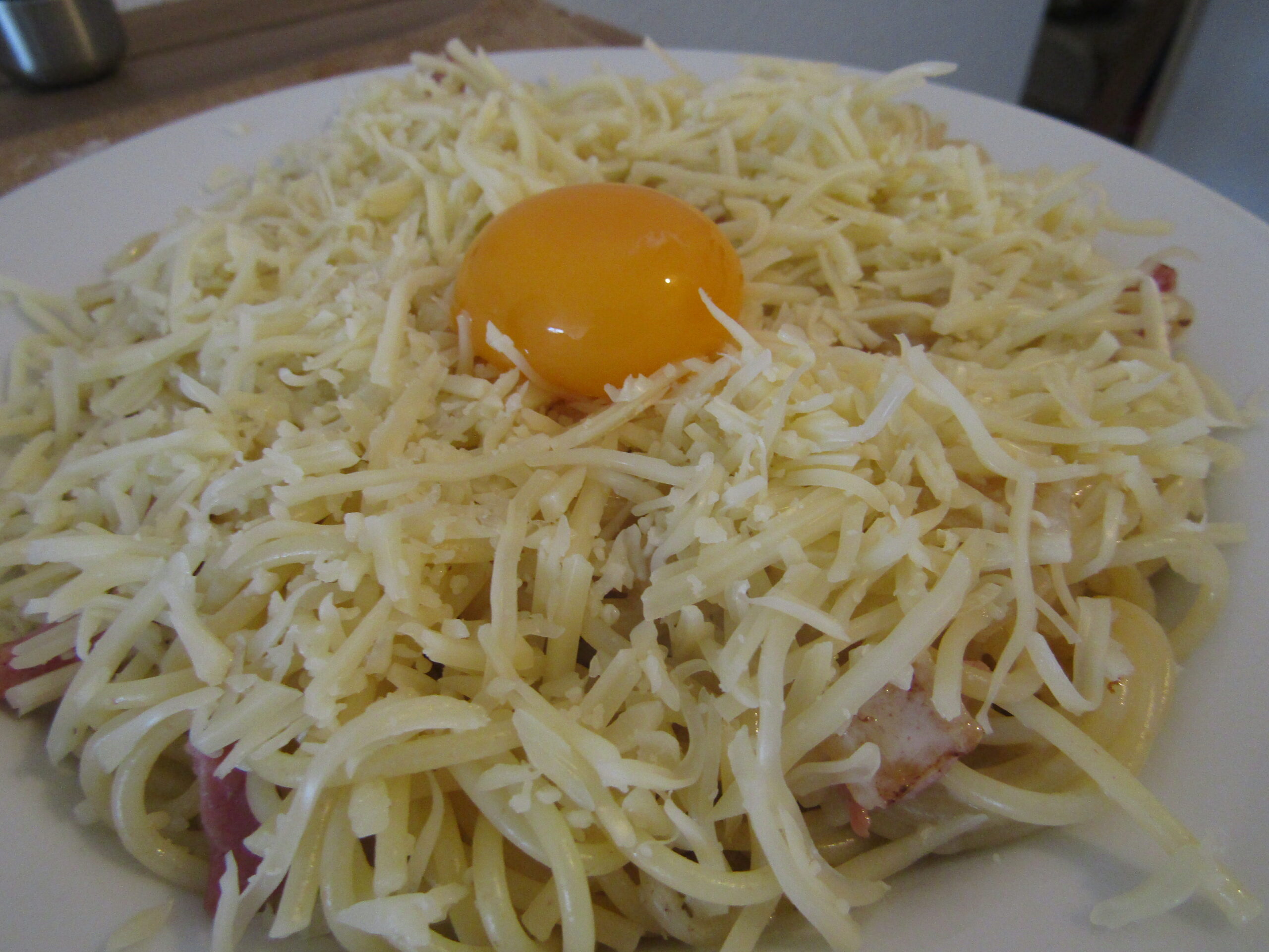 Un plat de spaghettis à la carbonara avec un œuf et du fromage râpé dessus.