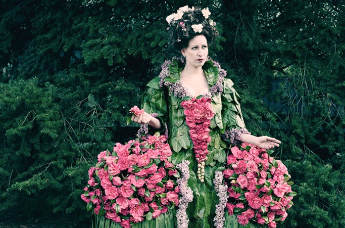 Photographie d'une personne portant une robe imposante et colorée, entièrement faite en fleurs et en feuilles. Le modèle porte aussi des fleurs dans les cheveux. Cette robe fait partie de la collection « Weedrobes ».