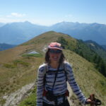 LIsl Weynans pose pour une photo. Elle est en randonnée dans la montagne. Elle porte une casquette et des lunettes. Elle sourit pour la caméra.