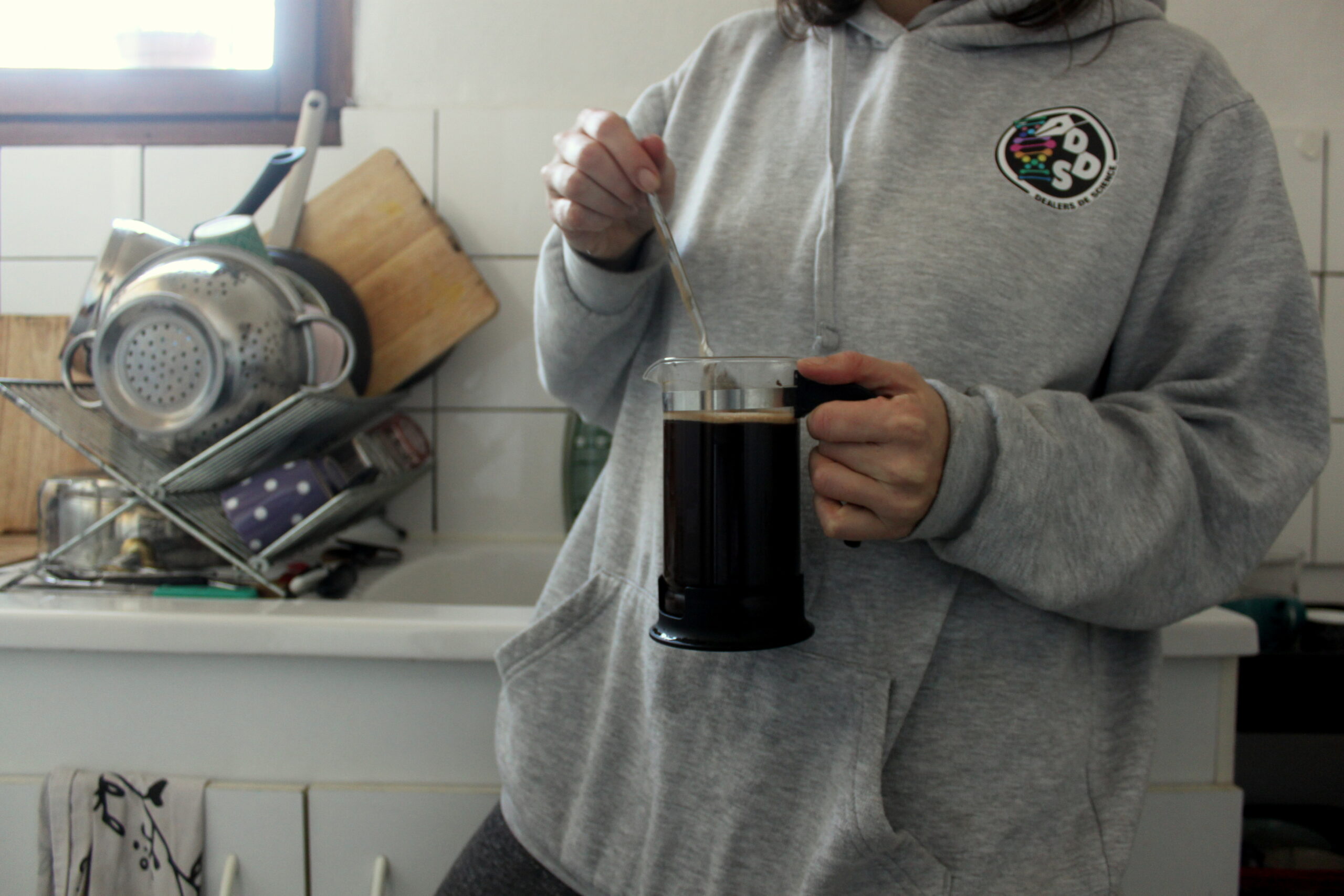 Nina est dans la cuisine. Elle porte un pull Dealers de Science et prépare du café.