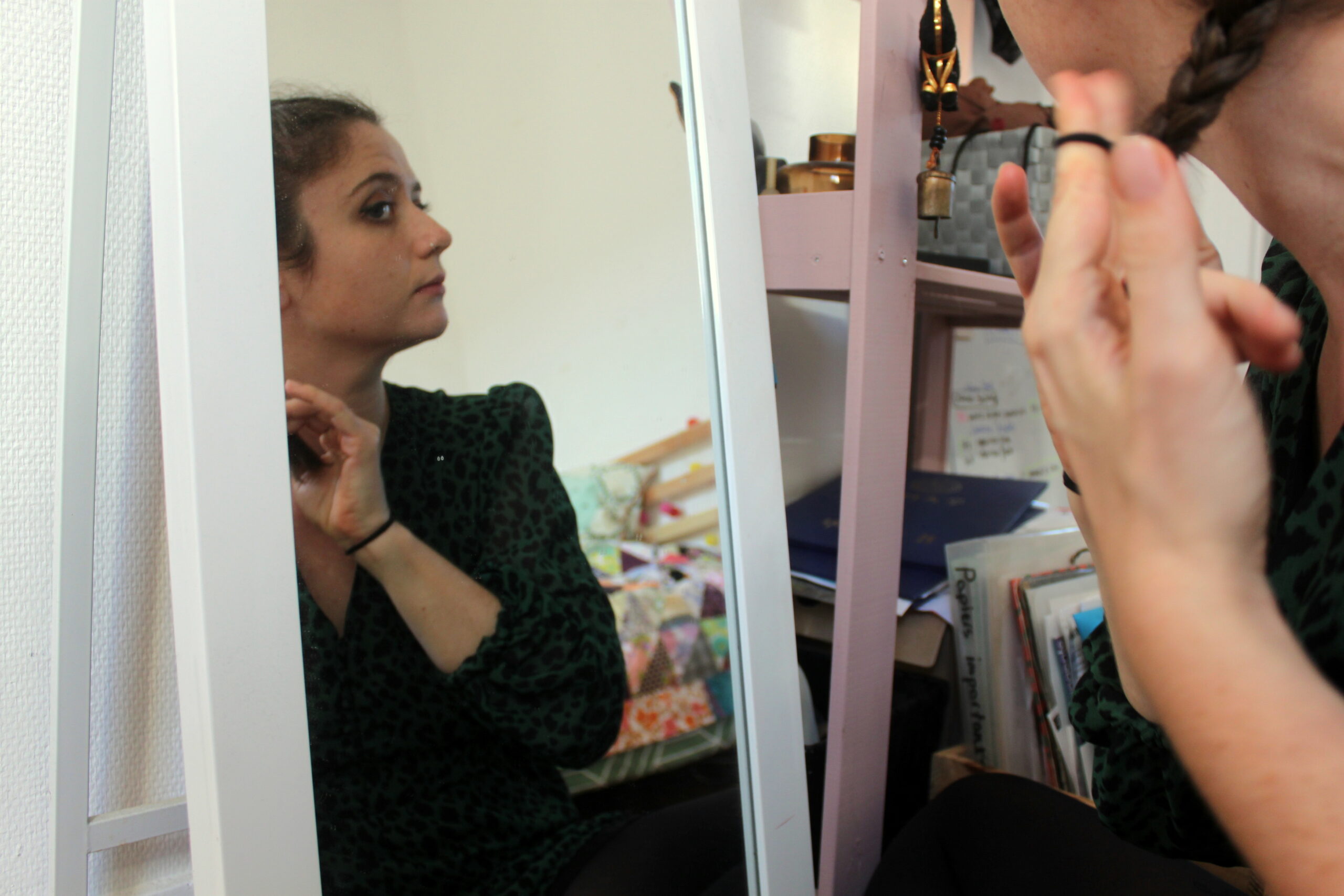 Nina se regarde dans le miroir pour se préparer. Elle se coiffe en se faisant des tresses.