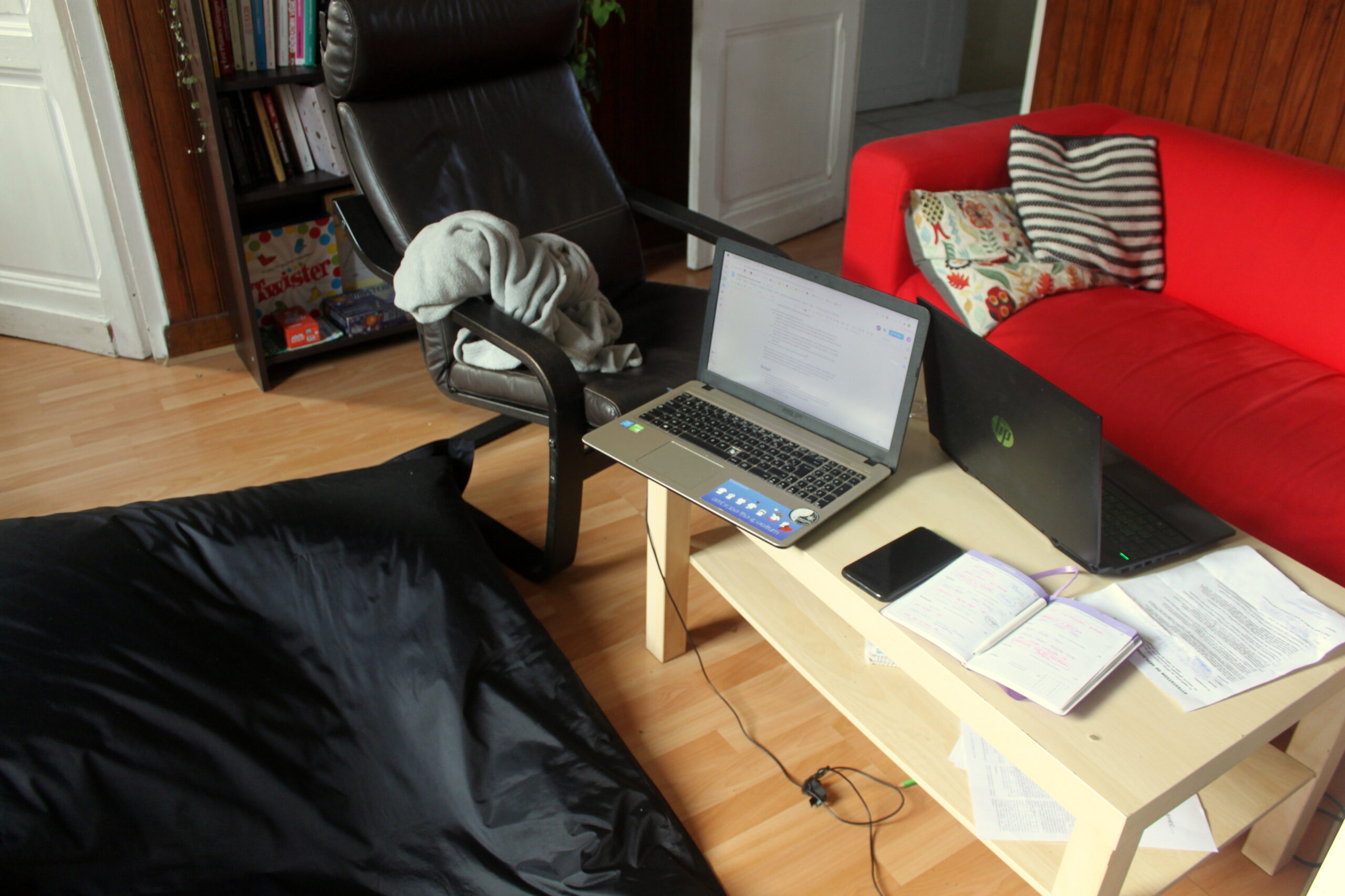 Le salon est devenu le bureau pour la journée. Sur la table basse il y a deux ordinateurs et un cahier.